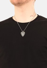 Collar de plata con forma de pua de guitarra, con diseño grabado. Llevado en una cadena sobre una camiseta negra.