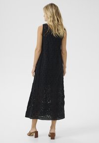 Black crochet maxi dress with circular patterns, sleeveless design, and intricate detailing, featuring a straight cut and mid-calf length.