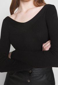 Zwart geribd topje met lange mouwen, een brede V-hals en aansluitende mouwen, gedragen met zwart, hoog getailleerd leren broek met knoopdetails.