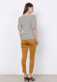 Prúžkovaný krémový a čierny top s nafúknutými rukávmi, spárovaný so žltými slim-fit nohavicami horčicovej farby. Čierne sandále na vysokom opätku dotvárajú celý outfit.
