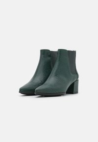 Bottines vertes en matériau texturé, dotées d'un talon bloc et de panneaux latéraux élastiques. Bout pointu et silhouette épurée.