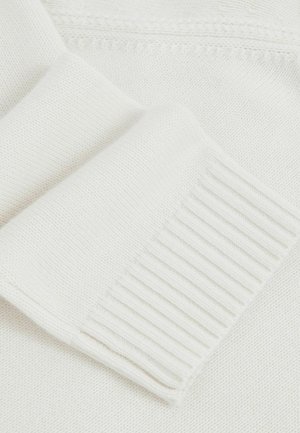 Közeli kép egy fehér kötött pulóver ujja rózsa bordázott mandzsettával és textúrált kötött anyaggal.