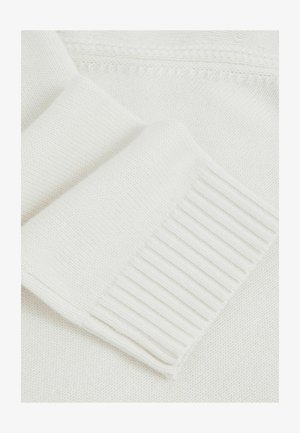 Közeli kép egy fehér kötött pulóver ujja rózsa bordázott mandzsettával és textúrált kötött anyaggal.