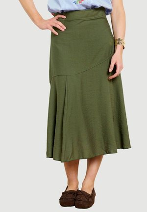 Femme portant une jupe midi vert olive à ourlet asymétrique, un chemisier rayé rentré, des mocassins marron à franges et un bracelet en or.
