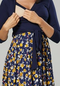 Navy dress with long sleeves and a floral skirt featuring yellow roses. Includes a wrap design and adjustable waist tie. Textured fabric.