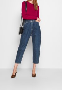 Denimbyxor med hög midja, lös passform, upprullade fållar, sidostråkar och en mörk tvätt. Kombineras med en lila långärmad top och klackar med leoprint.