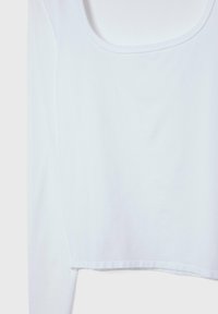 Crop top bianco a maniche lunghe realizzato in un tessuto morbido e leggero. Presenta un ampio scollo tondo e un orlo che si posiziona sopra la vita.