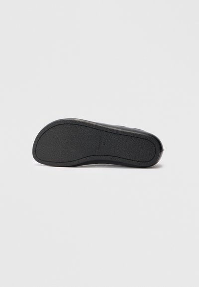 Suola nera di una scarpa con superficie in gomma texturizzata. Forma curva, bordi lisci e branding minimale. Progettata per grip e durata.