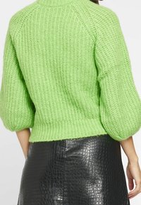 Grüner gestrickter Pullover mit geripptem Struktur und Puffärmeln, kombiniert mit einem schwarzen Rock aus Kunstleder im Krokodil-Look.