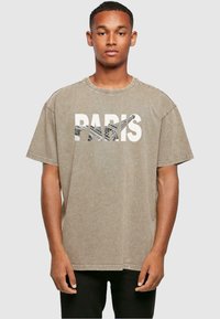 Beige oversized t-shirt med rund hals, med ordet "PARIS" i fede hvide bogstaver og en tekstureret grafik under.