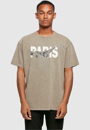 Beige Übergröße T-Shirt mit Rundhalsausschnitt, das das Wort "PARIS" in fetten weißen Buchstaben und eine strukturierte Grafik darunter zeigt.
