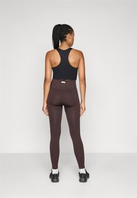 Fekete, racerback sportmelltartó, amelyet magas derékú, bordázott barna leggingsszel párosítottak. Az összeállítás sima textúrával és minimalista dizájnnal rendelkezik.