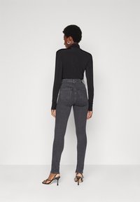 Black long-sleeve top paired with high-waisted grey jeans. Pants feature a slim fit and black heeled sandals. Simple, minimalist design.