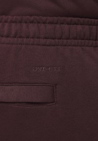 Burgundy joggerbyxor med en mjuk textur, elastisk midja och broderad "ORI-FIT" logotyp nära en sidoficka.