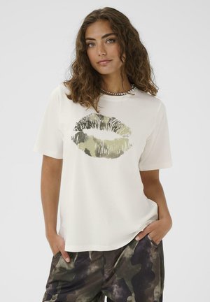 T-shirt blanc arborant une grande impression de lèvres métalliques dans des nuances d'or et d'olive. Manches courtes et coupe décontractée, associé à un pantalon camouflage.