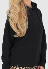 Felpa nera in tessuto morbido con tasca a marsupio. Presenta un cappuccio con coulisse e polsini a coste. Abbinata a leggings con stampa leopardata.
