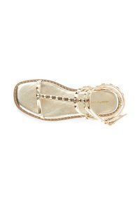 Sandal in oro con cinturini, dettagli borchiati, suola piatta e design superiore intrecciato; presenta una superficie liscia e metallica e una cinghia regolabile alla caviglia.