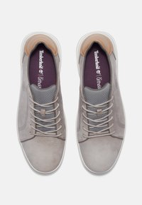 Grå mockaskor med en texturerad grå tåspets, bruna läderdetaljer och ljusgrå snörning. Mörklila innersulor och vita gummisulor.