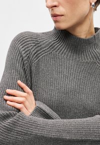 Maglione grigio lavorato a maglia con collo alto, caratterizzato da un design testurizzato, un motivo a coste e ampie maniche. Accentuato da una leggera lucentezza.