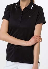 Černé polotričko s úzkým střihem, bílé detaily na límci a tříknoflíková léga. Měkk á, hladká textura. Jemné logo na hrudi.