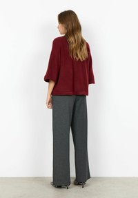 Top tricotat burgund cu mâneci largi, asortat cu pantaloni gri lejeri. Ansamblul are o croială relaxată și o textură subtilă. Pantofi cu imprimeu zebra.
