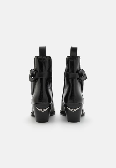 Bottines en cuir noir avec une finition brillante, dotées d'une sangle et d'une boucle, ainsi que des accents en métal en forme d'aile sur les talons.