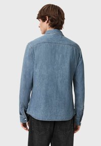 Lichtblauw denim overhemd met lange mouwen, een kraag en knoopmanchetten. Heeft een rugpas en een rechte zoom. Gelaagd stof.