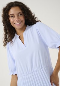 Svetlo modra nabirana obleka s kratkimi naborki in V-izrezom. Gladka tkanina z nabranim detajlom na pasu.