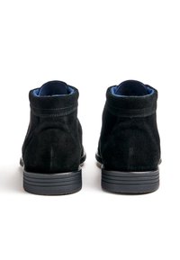 Bottes motardes en cuir suédé noir à finition texturée, semelles en caoutchouc plates et doublure intérieure contrastante bleue. Détails cousus apparents.