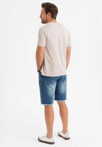 Ljusgrå t-shirt med kort ärm, ihop med blå denimshorts som slutar strax ovanför knäet. Skorna är vita sneakers med beige detaljer.