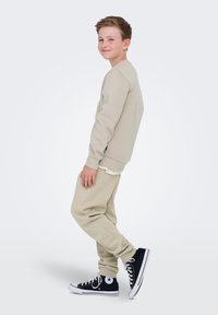 Beige katoenen sweatshirt en bijpassende aangesloten trainingsbroek met geribbelde boorden, gecombineerd met zwarte hoge sneakers met witte accenten.