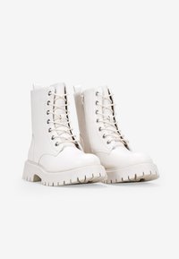 Stivali da combattimento bianchi con lacci, dotati di una suola in gomma spessa, finitura liscia, occhielli in argento e una cerniera laterale per indossarli facilmente.