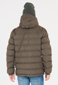 Brun puffjacka med huva, quiltat mönster och ribbade muddar. Matchad med ljusblå jeans och en grön mössa.
