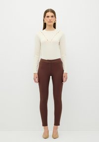 Romantop met lange mouwen in crèmekleur met V-hals en bruine strakke broek. Zachte textuur, slim fit en een hoge taille ontwerp. Neutraal gekleurde schoenen maken de outfit compleet.