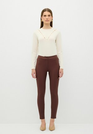 Romantop met lange mouwen in crèmekleur met V-hals en bruine strakke broek. Zachte textuur, slim fit en een hoge taille ontwerp. Neutraal gekleurde schoenen maken de outfit compleet.