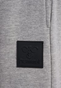 Gråt strikket stof med en tekstureret sort læderlap med præget logo og design, fastgjort til beklædningsgenstanden.