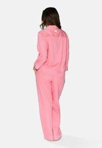 Roze pyjama set bestaande uit een knoopsluiting blouse met kraag en lange mouwen, en losse broek met zijzak en witte accentsteken.