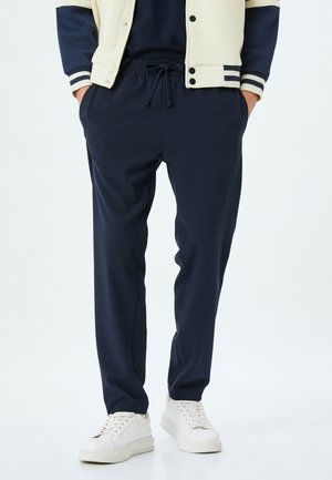 Pantalones de marine con cintura elástica y cordón ajustable, con bolsillos laterales. Combinados con zapatillas blancas sobre un fondo simple.