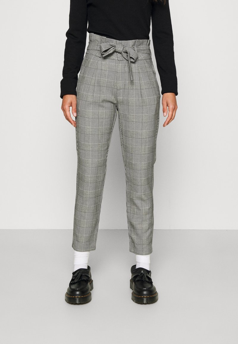 Plaid trousers in gray and black with a high waist and belt detail. Features tapered legs and worn with black shoes and white socks.