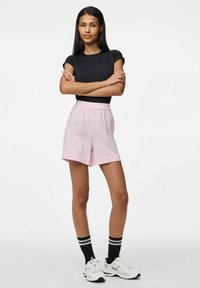 Svart kortärmad topp, rosa randiga shorts med elastisk midja, svarta randiga strumpor och vita sportskor. Slät textur.