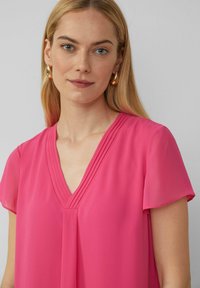 Kurze Ärmel, V-Ausschnitt Bluse in lebhaftem Pink, mit sanften Falten am Ausschnitt; aus leichtem, glattem Stoff gefertigt.