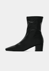 Μαύρο δερμάτινο μπότες μέσης γάμπας με μυτερή μύτη και χοντρό τακούνι σε απλό ανοιχτό γκρι φόντο, πλάγια όψη.