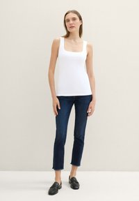 White ribbed tank top with a square neckline, paired with dark blue ankle-length jeans featuring a frayed hem, and black loafers.