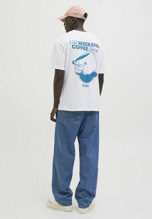Witte katoenen t-shirt met een blauw grafisch ontwerp op de achterkant, gecombineerd met losse blauwe denim jeans en een lichtroze pet.