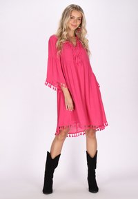 Rochie roz, până la genunchi, cu mâneci evazate și accente cu ciucuri la tiv. Fabricată dintr-un material ușor, având un decolteu în V și o croială lejeră.