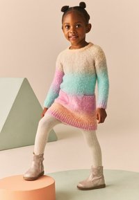 Robe en tricot multicolore avec des dégradés de rose, bleu et crème ; deux poches à l'avant. Associée à des collants texturés crème et des bottes grises.