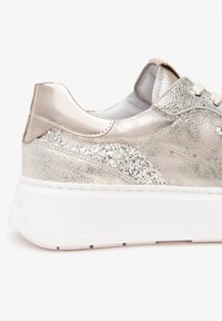Metallisch silberner Sneaker mit strukturiertem Material und einem Glitzerakzent an der Seite. Verfügt über eine weiße Plateausohle und eine glatte, metallische Ferse.