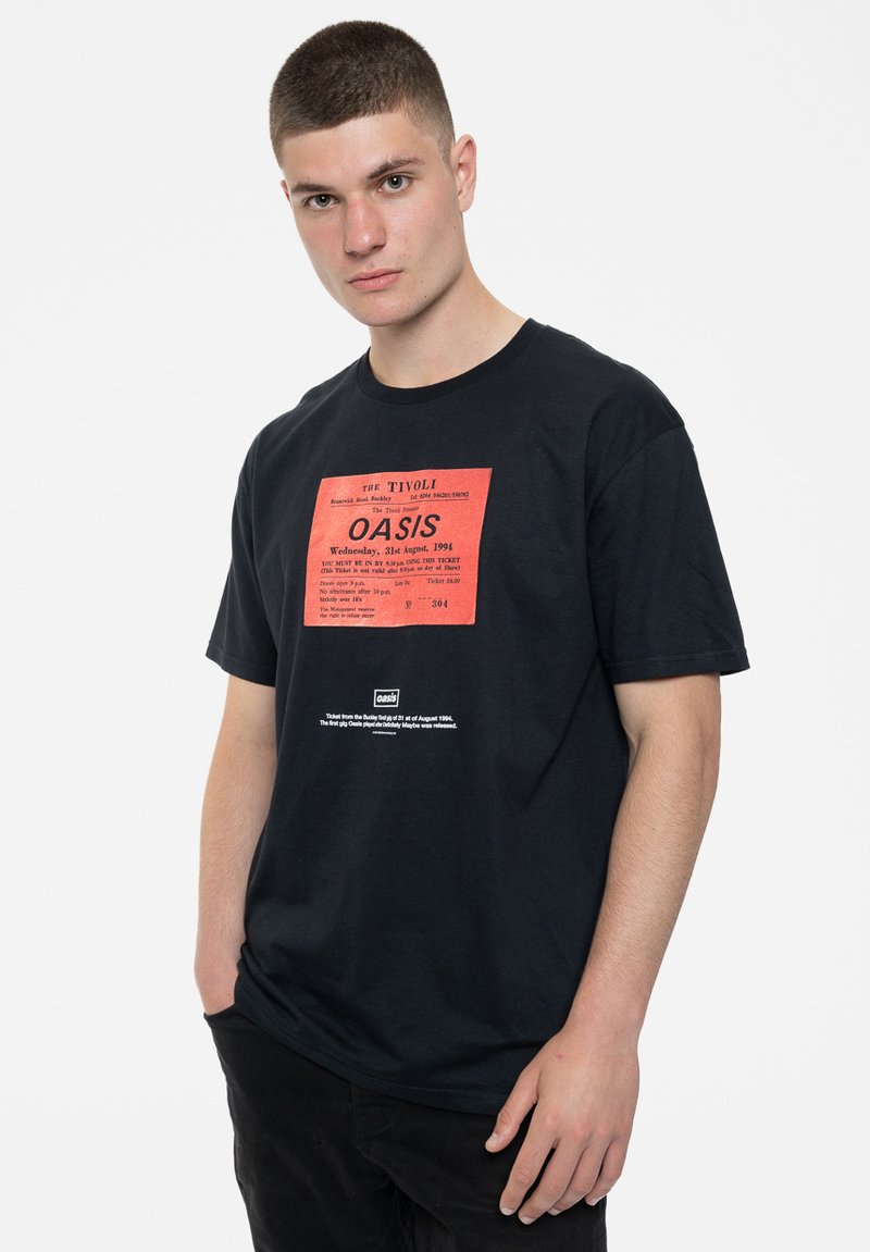 Black cotton t-shirt featuring a red graphic print resembling a concert ticket for Oasis with text; relaxed fit, short sleeves, and crew neck.