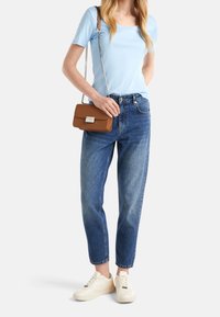 Světlomodré tričko s krátkým rukávem, středně modré džíny s rovnými nohavicemi, krémové tenisky a hnědá kabelka přes rameno se stříbrnou sponou.