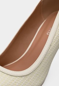 Κοντινό πλάνο μπεζ πλεγμένου επίπεδου παπουτσιού με εκρού περιμετρική λεπτομέρεια και ανοιχτό καφέ εσωτερική σόλα.